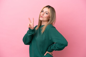 Young caucasian woman isolated on pink background smiling and showing victory sign