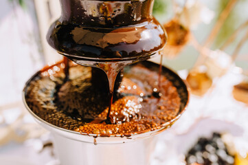 Hot brown milk melted chocolate pours over the tiers of the fountain close-up at the celebration...