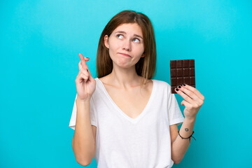 Young English woman with chocolat isolated on blue background with fingers crossing and wishing the best