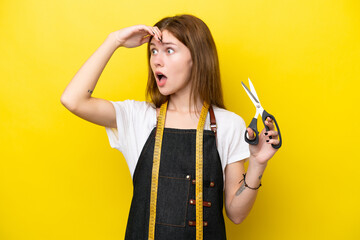 Young seamstress English woman isolated on yellow background doing surprise gesture while looking...