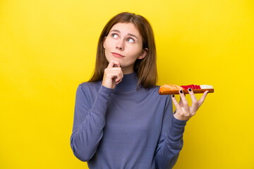 Young English woman holding sashimi isolated on yellow background and looking up