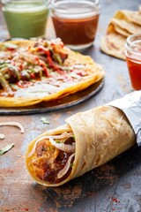 Kati roll with meat on a table against an open roll and sauces in the background