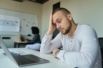 Fototapeta premium Tired man in a white shirt sitting at his desk