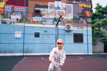 Little girl stands against the background of a basketball hoop on a multi-colored wall at home. High quality photo