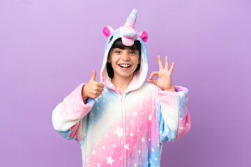 Little kid wearing a unicorn pajama isolated on purple background showing ok sign and thumb up gesture