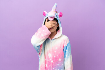 Little kid wearing a unicorn pajama isolated on purple background covering eyes by hands. Do not want to see something