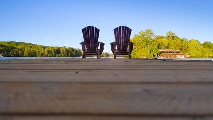 Two empty Adirondack chairs sitting on a dock on a lake in Muskoka, Ontario Canada. Calm morning on...