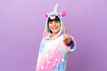Little kid wearing a unicorn pajama isolated on purple background showing and lifting a finger
