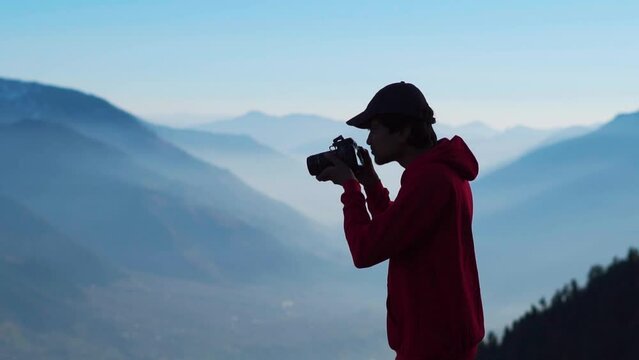 Silhouette shot of an Indian photographer taking photo in front of the foggy Himalayan mountains at Manali in Himachal Pradesh, India. Traveler taking photo of mountains. Man shoots landscape. 