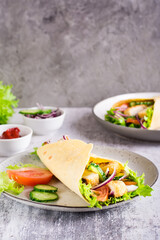 Mexican tortilla wraps with  vegetables and chicken on a plate on the table. Vertical view