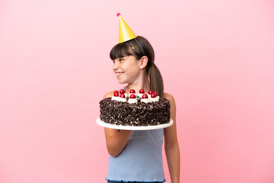 Little caucasian kid holding birthday cake isolated in pink background looking side