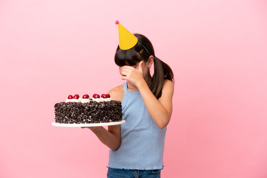 Little caucasian kid holding birthday cake isolated in pink background laughing