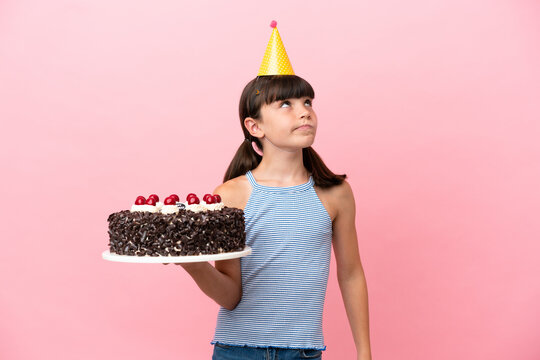 Little caucasian kid holding birthday cake isolated in pink background and looking up
