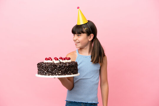 Little caucasian kid holding birthday cake isolated in pink background looking to the side and smiling