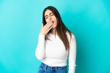 Young caucasian woman isolated on blue background yawning and covering wide open mouth with hand