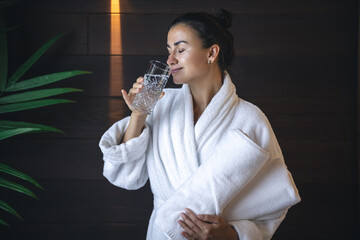 A young woman with a glass of water after the sauna is resting.
