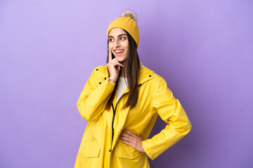 Young caucasian woman wearing a rainproof coat isolated on purple background thinking an idea while looking up