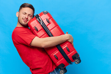 Enjoyed joyful tanned handsome man in red t-shirt hugging with suitcase waiting impatiently for...