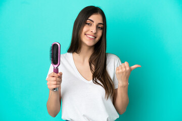 Young caucasian woman with hair comb isolated on blue background pointing to the side to present a product