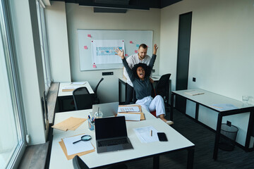 Man in office pushes joyful multiracial woman in armchair