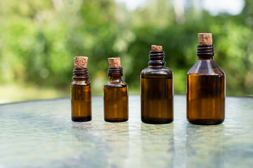 Small brown glass medicine bottles on glass table with green outdoor  background. Essential oil. 