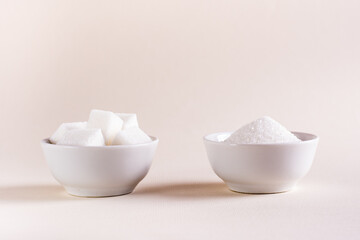 Sugar cubes and granulated sugar in bowls on a light background. Choosing between types of sugar