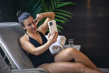 A young woman is relaxing in a spa complex and using a smartphone.