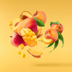 Fresh ripe whole and sliced mango and peaches with green leaves falling in the