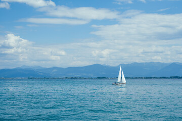 W boat with white sails on the bodensee in Switzerland. It is a sunny day with a blue sky. 