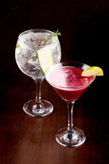 mixology two cocktail glasses with martini, berries, gin, cucumber, rosemary, ice on wooden table