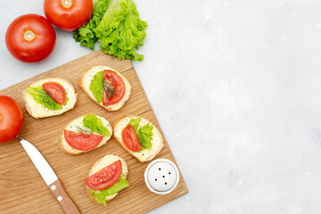 Bruschetta sandwich bread toast with soft white cheese ricotta,fresh tomatoes,basil greenery on a wooden cutting board.Tasty healthy vegetarian food,Italian cuisine appetizer. top view flat lay