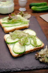 Bruschetta sandwich bread toast with soft green avocado cheese ricotta,fresh cucumbers,basil greenery on wooden cutting board.Tasty healthy vegetarian food,Italian cuisine appetizer.top view flat lay