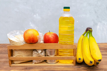 Donation food box, volunteering help,humanitarian aid full of canned,sunflower oil, pasta,cereal,grain and apples,banana,fruits. Delivery wooden box for charity on gray, wooden background still life