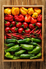 Different types and colors of peppers arranged in a wooden container, top view