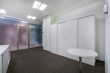 A bright office space with a glass wall, gray carpet and white wardrobe.