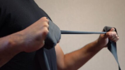 Male hands stretch a rubber band. Fitness workout. compression and stretching of the elastic band. Dark skin. Black T-shirt. Part of the body. No face.