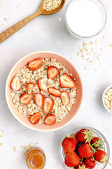 Oatmeal porridge with summer strawberries berries. Porridge oats in bowl with honey,milk,nuts. Healthy food breakfast,lifestyle,dieting, proper nutrition. Top view flat lay on gray table background