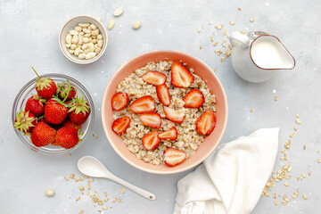 Oatmeal porridge with summer strawberries berries. Porridge oats in bowl with milk,nuts. Healthy food breakfast,lifestyle,dieting, proper nutrition. Top view flat lay on gray table background