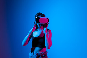 Young brunette woman in black t-shirt wearing a VR headset and looking up while playing a game with...