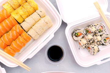 Set of fish sushi rolls with salmon and sesame,ginger,wasabi,soy sauce packed in plastic disposable container box on gray background.Seafood,Food delivery,take out service from restaurant concept