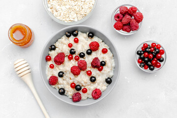 Oatmeal porridge with summer raspberry, currant berries,honey. Porridge oats in bowl with fruits. Healthy food breakfast,lifestyle,dieting, proper nutrition.Top view flat lay on gray table background
