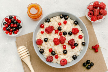 Oatmeal porridge with summer raspberry, currant berries,honey. Porridge oats in bowl with fruits. Healthy food breakfast,lifestyle,dieting, proper nutrition.Top view flat lay on gray table background