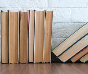 A stack of hardcover books on a wooden table against a white brick wall