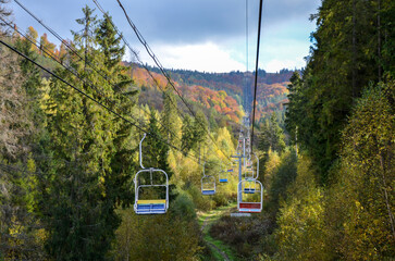 Empty aerial chair lift through colorful foliage in the autumn mountain forest 