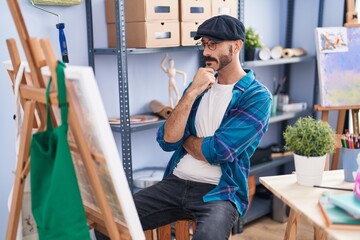 Young hispanic man artist looking draw with doubt expression at art studio