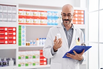 Naklejka na ściany i meble Young hispanic man pharmacist holding clipboard and pills at pharmacy