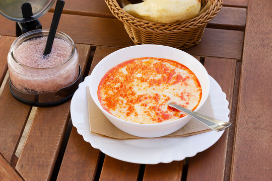 Bowl of traditional Balkan tripe soup, stew called Shkembe Chorba is made of tripe, cow or lamb stomach, wooden table, popular in Turkey and Macedonia, served with pickled garlic