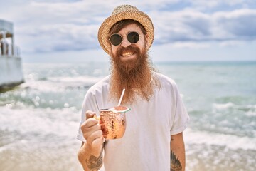 Young redhead man smiling happy drinking cocktail at the beach.