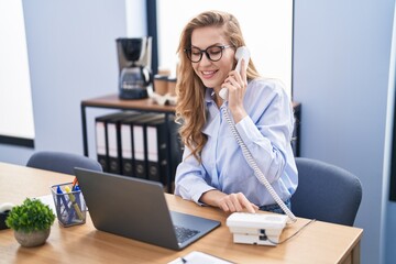 Young blonde woman business worker using laptop talking on the telephone at office