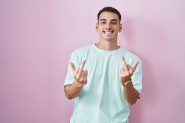 Handsome hispanic man standing over pink background showing middle finger doing fuck you bad...
